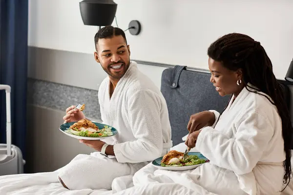 A joyful couple shares a delightful meal in cozy robes, basking in beautiful moments during their vacation. — Stock Photo