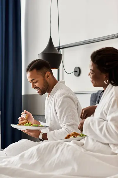 A young couple shares laughter and love while enjoying a cozy meal in their hotel room. — Stock Photo