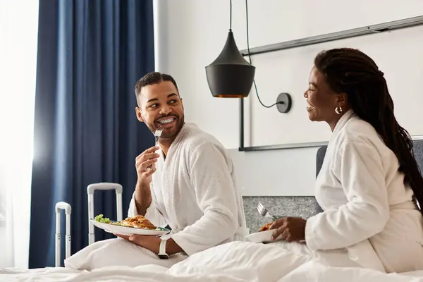 Ein fröhliches Paar teilt ein köstliches Frühstückserlebnis in seinem gemütlichen Hotelzimmer, das Liebe und Verbundenheit ausstrahlt. — Stockfoto