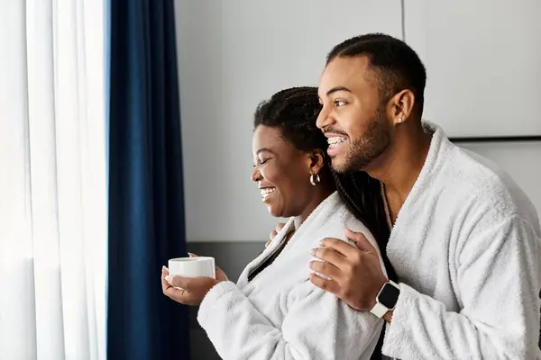 A joyful couple shares a tender moment, sipping warm drinks and embracing in their hotel room. — Stock Photo