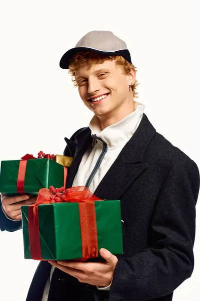 A young man exudes holiday cheer, holding two beautifully wrapped gifts adorned with colorful ribbons. — Stock Photo