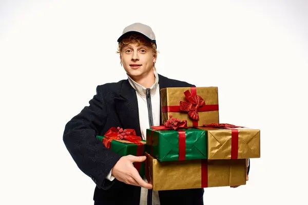 Un jeune homme vêtu d'une tenue de vacances élégante présente un look joyeux tout en portant un assortiment de cadeaux de Noël emballés. — Photo de stock