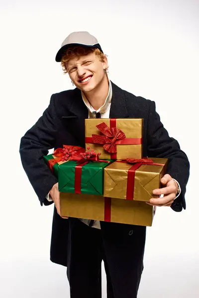 A cheerful man showcases his trendy holiday fashion while joyfully holding a stack of beautifully wrapped Christmas presents adorned with ribbons. — Stock Photo