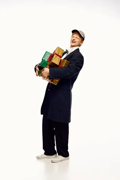 Em um clima festivo, um homem mostra trajes elegantes como ele equilibra uma pilha de presentes de Natal coloridos. — Fotografia de Stock