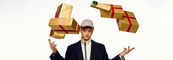 A fashionable man expertly juggles beautifully wrapped gift boxes adorned with red ribbons, creating a festive atmosphere. — Stock Photo