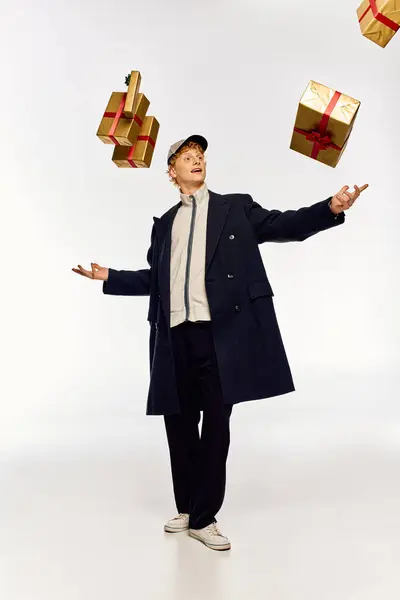 In a fashion forward display of holiday cheer, a man confidently juggles wrapped Christmas presents while dressed in an elegant coat. His playful attitude embodies the joy of the season. — Stock Photo