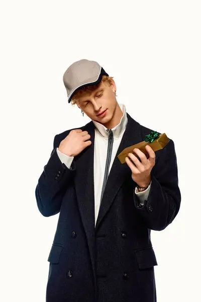 Un uomo alla moda è vestito con un abito invernale chic, tenendo un regalo ben avvolto mentre lo guarda con attenzione.. — Foto stock