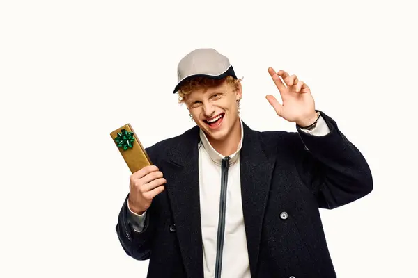 A man showcases his holiday spirit in stylish attire, holding a beautifully wrapped gift. The joyful expression and cheerful wave reflect the excitement of Christmas 2025 festivities. — Stock Photo