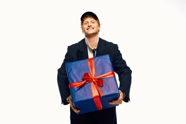 Smiling man dressed in trendy holiday fashion presents a beautifully wrapped gift, capturing the festive spirit of Christmas 2025. — Stock Photo