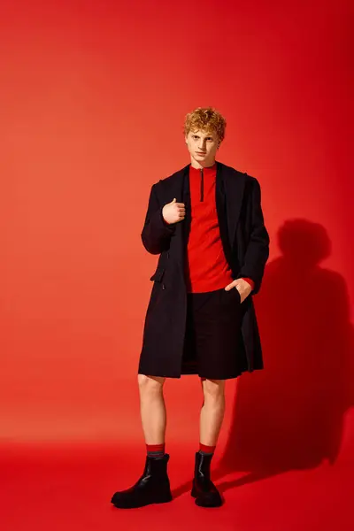A stylish man showcases holiday fashion for 2025 with a striking red sweater and a sleek black coat. — Stock Photo