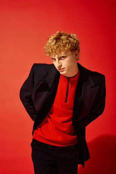 Um jovem em uma roupa vermelha impressionante combina elegância moderna com toque festivo, posando com confiança contra um fundo vermelho ousado. Seu cabelo encaracolado adiciona um toque brincalhão ao conjunto sofisticado. — Fotografia de Stock