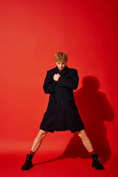 Stylish man showcases bold holiday fashion in a dramatic pose against a vibrant red background. — Stock Photo