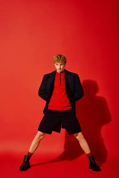 A fashionable man stands confidently in a striking red setting, showcasing a modern holiday outfit. His unique ensemble blends casual and chic elements, perfect for festive gatherings in 2025. — Stock Photo