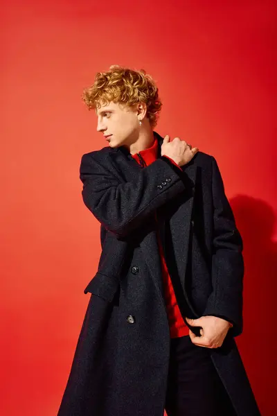 In a festive setting, a man presents his holiday style by wearing a chic coat over a bright red sweater. — Stock Photo