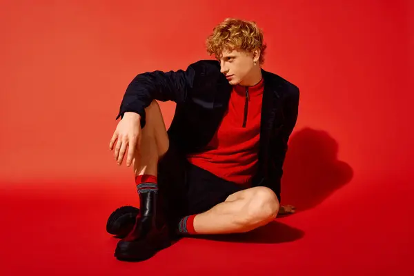 A fashionable man sits on the floor against a vivid red backdrop, combining modern holiday style with vibrant colors. — Stock Photo