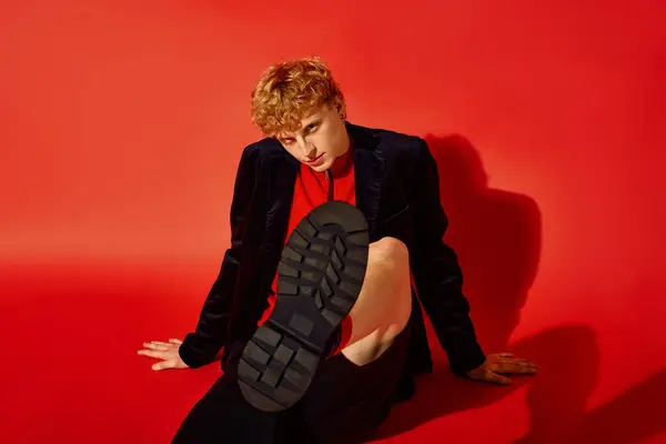 A young man showcases his unique holiday outfit against a bright red backdrop. Dressed in a stylish combination, he confidently poses, embodying the spirit of Christmas 2025 with flair. — Stock Photo