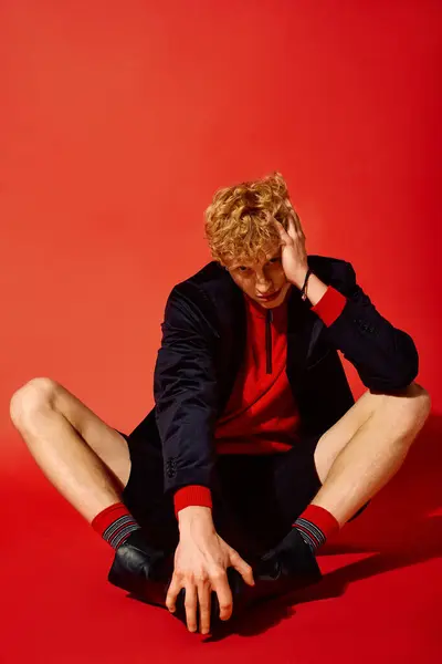 A fashionable man poses in a striking red environment, dressed in a festive outfit perfect for Christmas 2025. — Stock Photo