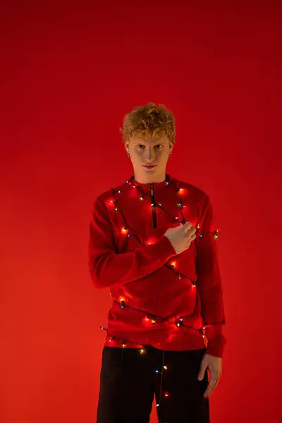 A young man showcases his unique sense of style this holiday season by wearing festive red attire adorned with colorful Christmas lights. — Stock Photo
