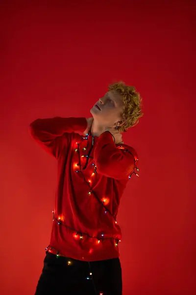 A fashionable man showcases his unique holiday style against a vibrant red backdrop, adorned with colorful Christmas lights. — Stock Photo