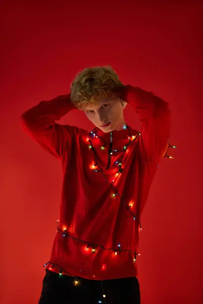 A young man showcases his stylish holiday outfit adorned with colorful Christmas lights against a vibrant red backdrop. This festive arrangement captures the essence of Christmas cheer in 2025. — Stock Photo