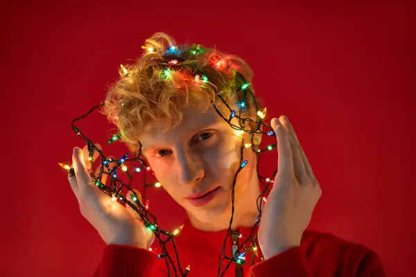 A stylish young man showcases his creativity by wrapping colorful holiday lights around his head. — Stock Photo