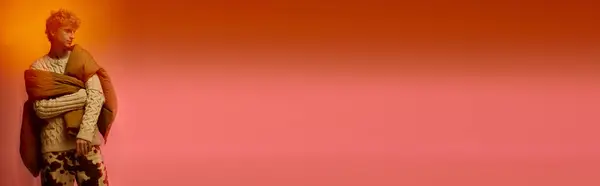 A stylish man showcases holiday fashion with an eye catching outfit, wrapped in cozy layers against a bold orange and pink backdrop, embodying the festive spirit of Christmas 2025. — Stock Photo
