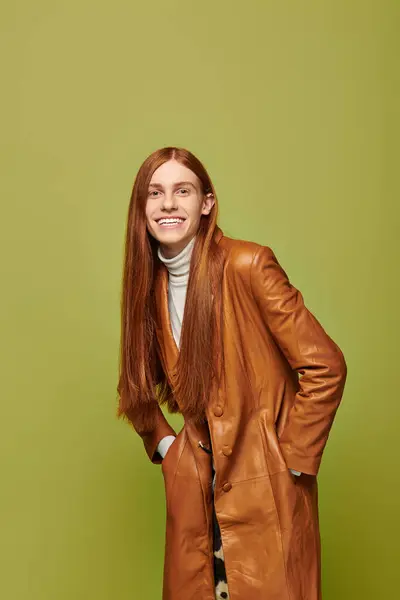 A young man with long red hair expresses his emotions joyfully in a lively green background. — Stock Photo