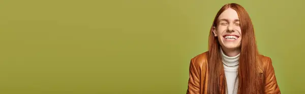 Emotional young man with long red hair smiles brightly in a warm and vibrant setting. — Stock Photo