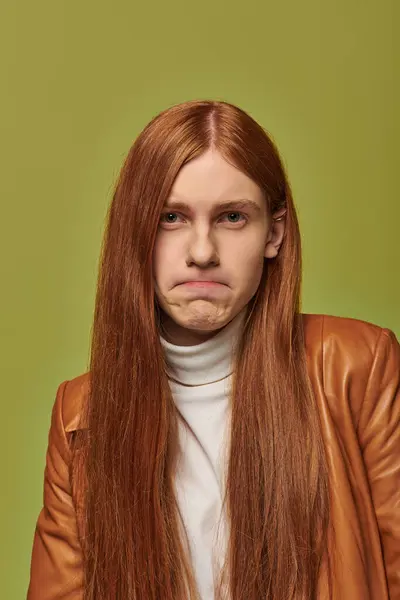 Un joven con el pelo largo y rojo muestra emociones profundas sobre un fondo verde brillante. — Stock Photo