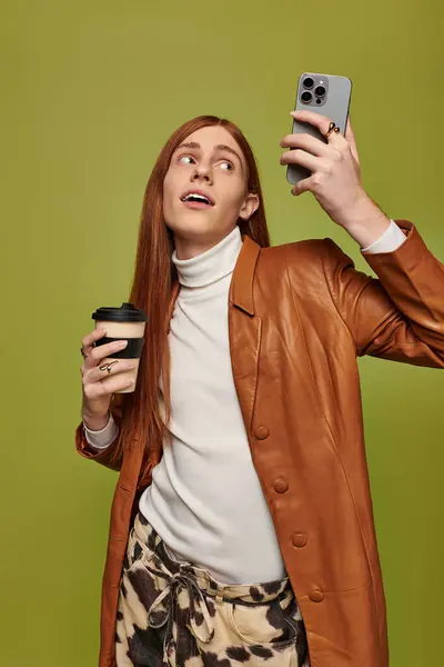 Giovane uomo con lunghi capelli rossi cattura le sue emozioni mentre si gode un caffè e uno smartphone. — Foto stock