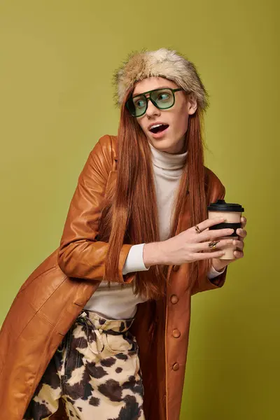 Emotionally engaged young man with long red hair holds a coffee cup, showcasing playful vibes. — Stock Photo