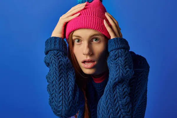 Un joven con el pelo rojo largo en un gorro de color rosa brillante muestra una gama de emociones contra el azul. — Stock Photo