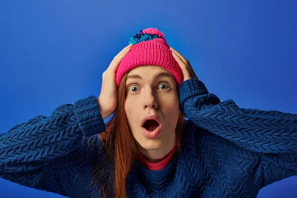 Emotional young man with long red hair shows shock while wearing a colorful beanie. — Stock Photo