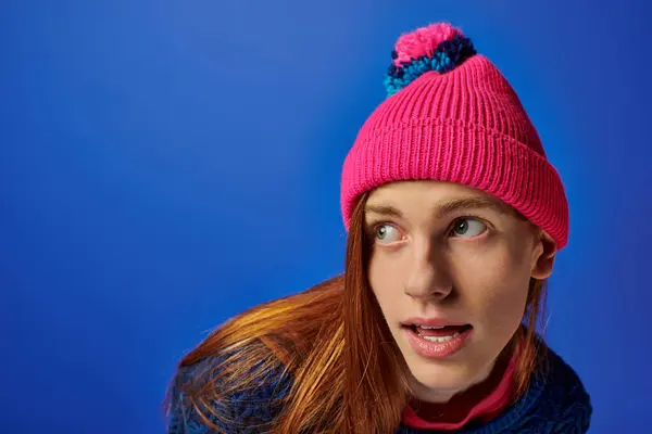 Emotional young man with long red hair wears a bright pink hat and colorful sweater. — Stock Photo
