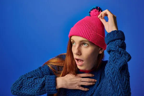 Emotional young man with long red hair expresses astonishment while wearing a pink beanie. — Stockfoto