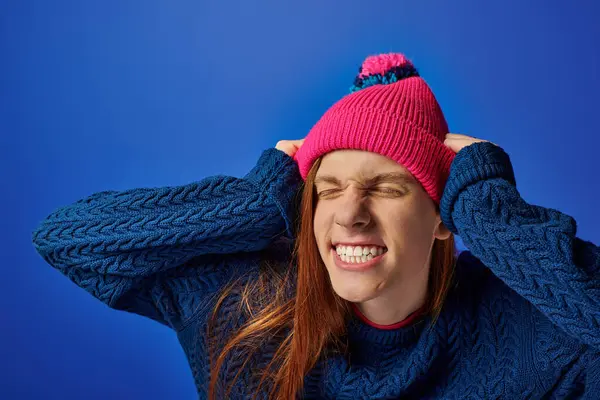 Le jeune homme exprime des émotions intenses tout en tenant sa tête, vêtu d'un pull vibrant et d'un chapeau. — Photo de stock