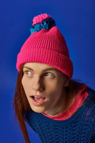 A young man with long red hair shows a surprised expression while wearing a colorful beanie. — Stock Photo