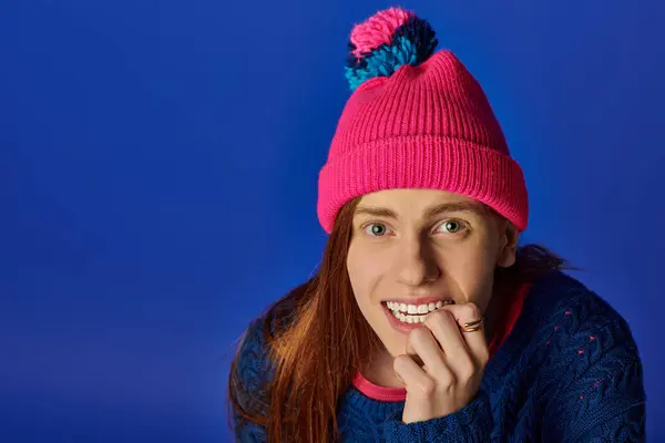 Young man with long red hair smiles warmly while wearing a colorful winter hat and sweater. — Stock Photo