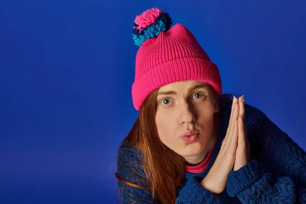 Emotional young man with long red hair showcases a playful expression against a blue background. — Stock Photo