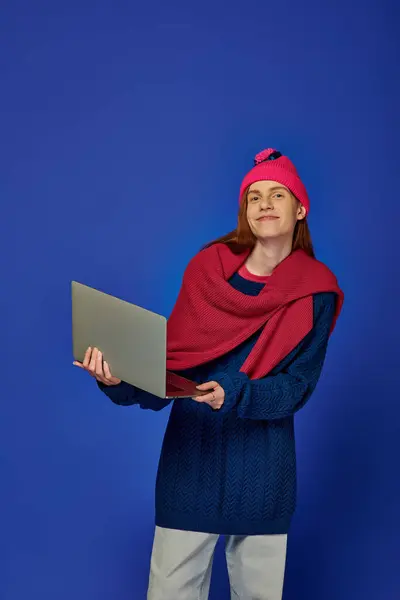 A young man with long red hair engages with his laptop in a vibrant, colorful setting. — Stock Photo