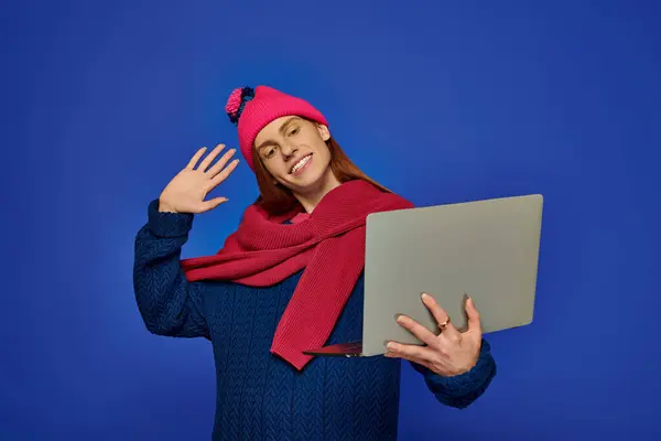 Um homem jovem com longas ondas de cabelo vermelho e sorrisos enquanto se envolve com seu laptop, mostrando alegria. — Fotografia de Stock