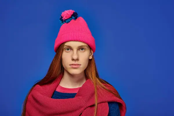 A young man with long red hair in a pink hat displays strong emotions by a blue wall. — Stock Photo
