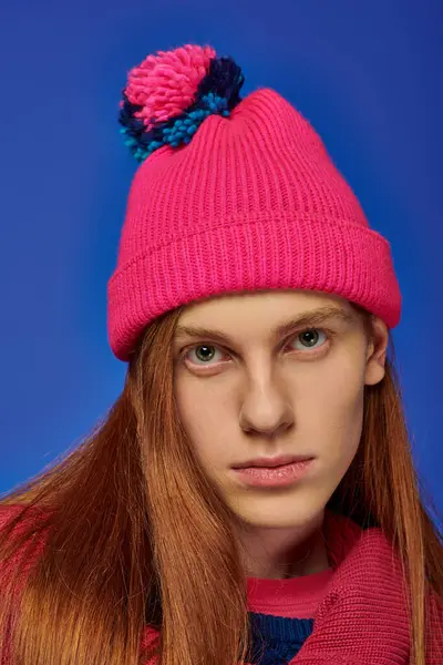 A young man with long red hair and a colorful beanie shows deep emotions against a vivid backdrop. — Stock Photo