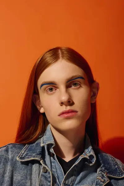 A young man with striking long red hair expresses deep emotions in front of an orange wall. — Stock Photo