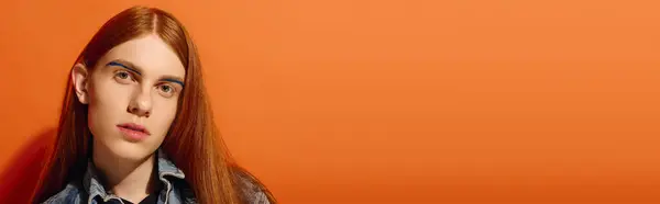 Un joven con el pelo rojo largo muestra una gama de emociones en un entorno naranja vivo. - foto de stock