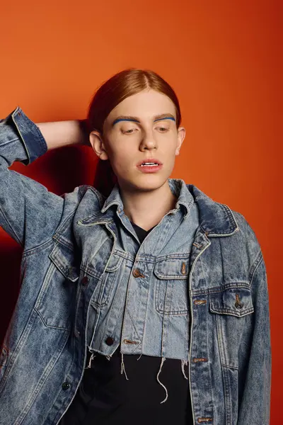 Hombre joven con el pelo largo y rojo muestra emociones profundas mientras posa frente a un telón de fondo naranja. - foto de stock