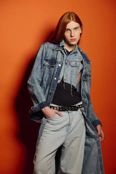 Young man with long red hair shows emotion in denim against vibrant colors. — Stock Photo