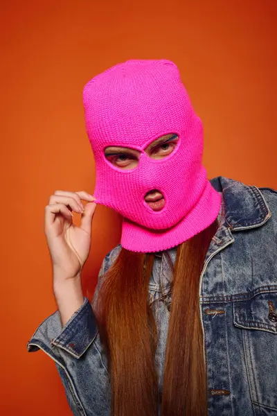 A young man with long red hair displays strong emotions behind a vibrant pink mask. — Stock Photo