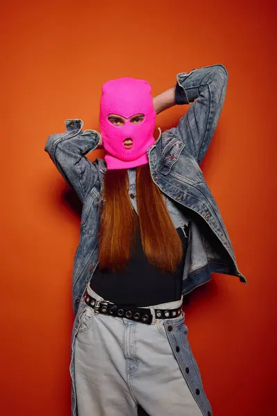 Young man with long red hair and a pink ski mask poses against a vibrant backdrop. — Stock Photo