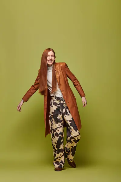 A young man with long red hair expresses emotions in a stylish outfit against a green backdrop. — Stock Photo